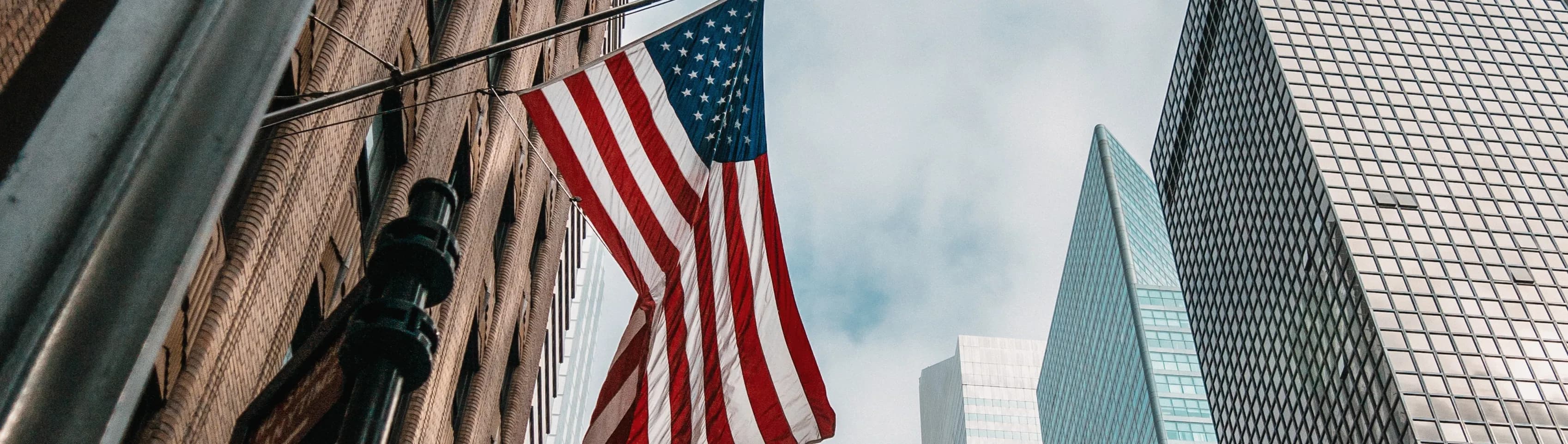 1792660039067-HERO-usa-united-states-america-flag-flagpole-near-skyscrapers-cloudy-sky.webp
